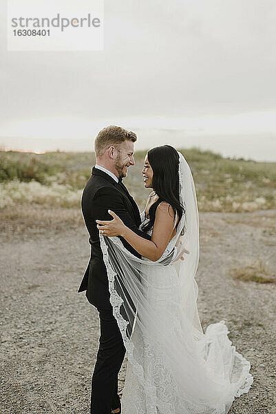 Lächelnde Braut und Bräutigam schauen sich im Feld gegen den Himmel an