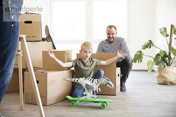 Mann packt Kartons aus  während sein Sohn in der neuen Wohnung mit Spielzeug spielt