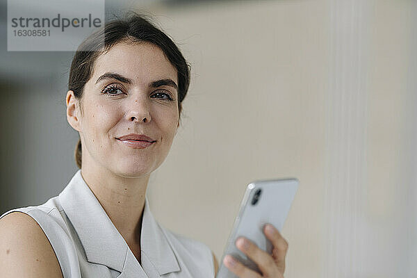 Lächelnde Frau  die ein Handy hält  während sie im Büro steht