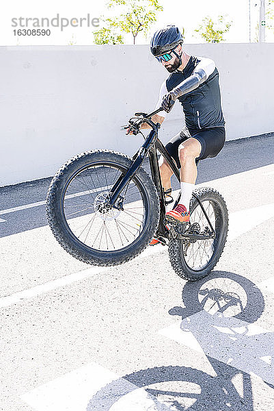 Männlicher amputierter Sportler  der an einem sonnigen Tag einen Stunt mit dem Fahrrad auf der Straße vollführt