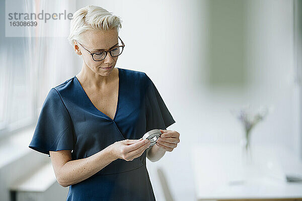 Geschäftsfrau mit Brille  die ein Objekt betrachtet  während sie im Büro steht