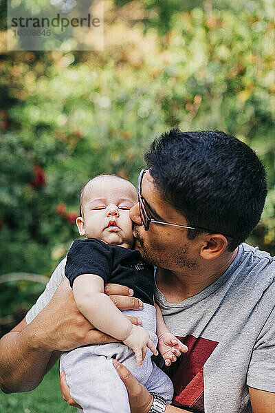 Junger Mann küsst süßen Sohn im Park am Wochenende
