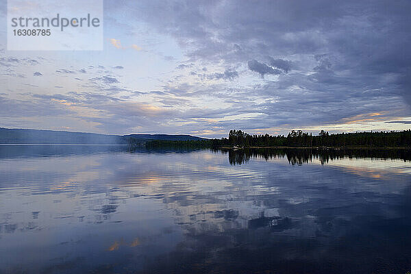 Schweden  Stroemsund  Sonnenuntergang an einem See und Rauch von einem Lagerfeuer