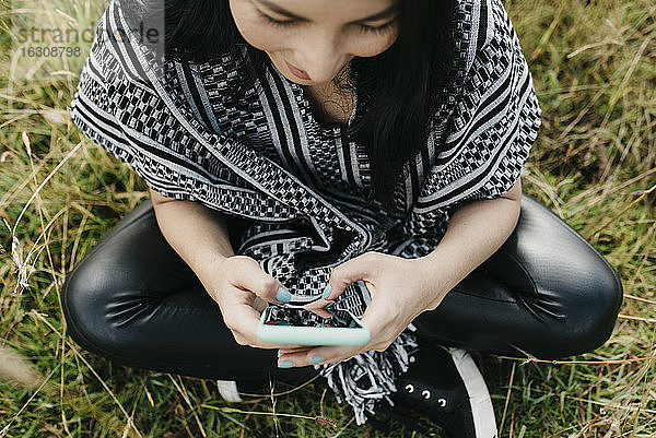 Frau schreibt Textnachrichten auf ihrem Smartphone  während sie in einem öffentlichen Park sitzt