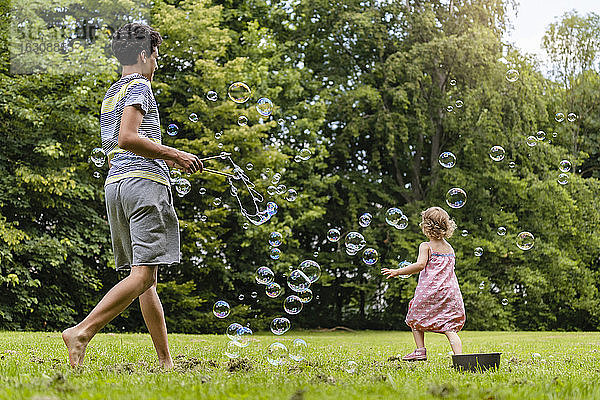 Bruder und Schwester spielen mit Seifenblasen im Park
