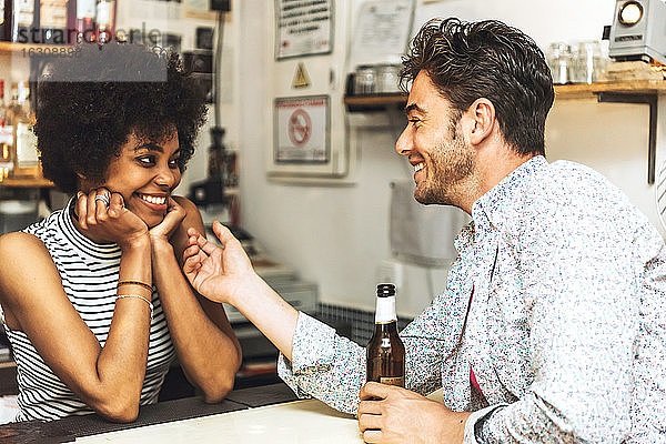 Mann hält Bierflasche und berührt Barkeeperin  während er mit ihr an der Theke flirtet