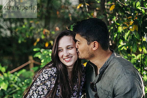Junger Mann mit geschlossenen Augen küsst lächelnde Frau im Park