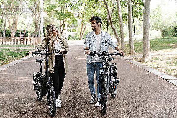Lächelndes junges Paar mit Elektrofahrrädern auf der Straße