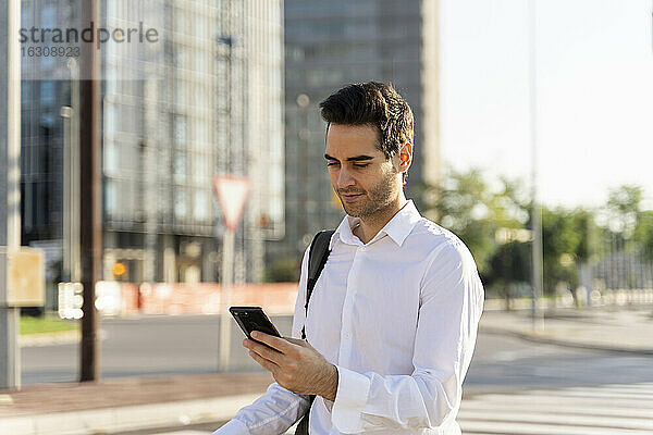 Geschäftsmann  der ein Smartphone benutzt  während er auf der Straße in der Stadt steht