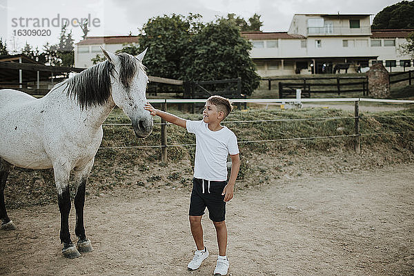 Junge  der ein weißes Pferd streichelt  während er in der Scheune steht