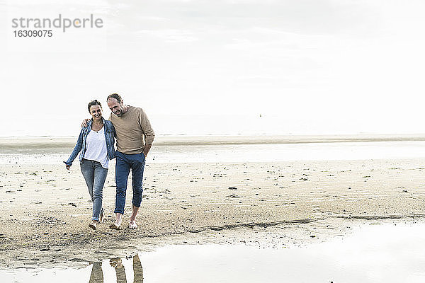 Lächelnd reifen Paar zu Fuß am Strand gegen den Himmel bei Sonnenuntergang