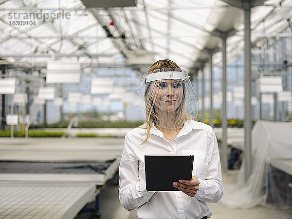 Geschäftsfrau mit Gesichtsschutz und digitalem Tablet bei der Arbeit in einer Gärtnerei