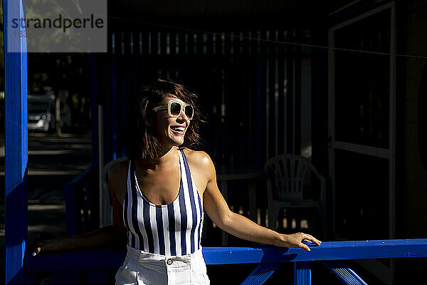 Fröhliche Frau schaut weg  während sie an einem sonnigen Tag an einem Geländer steht