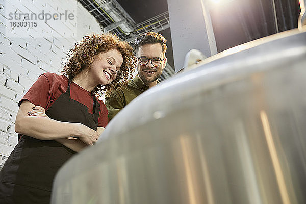 Mann und Frau arbeiten in einer Handwerksbrauerei und schauen in den Tank