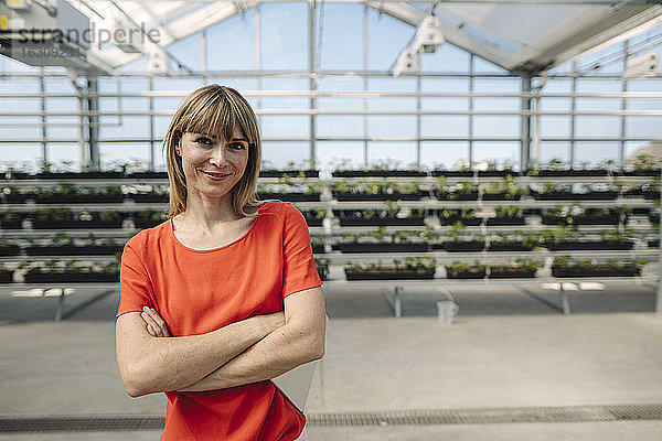 Lächelnde Unternehmerin mit verschränkten Armen  die vor Pflanzen in einer Gärtnerei steht