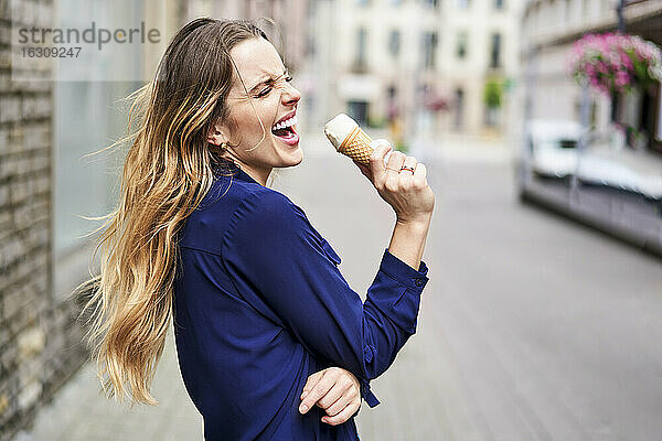 Fröhliche Frau isst Eis auf einem Fußweg in der Stadt