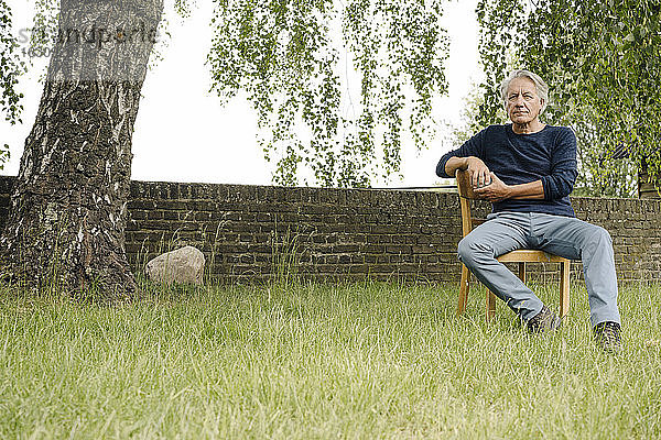 Nachdenklicher Mann sitzt auf einem Stuhl an einer Backsteinmauer im Hinterhof