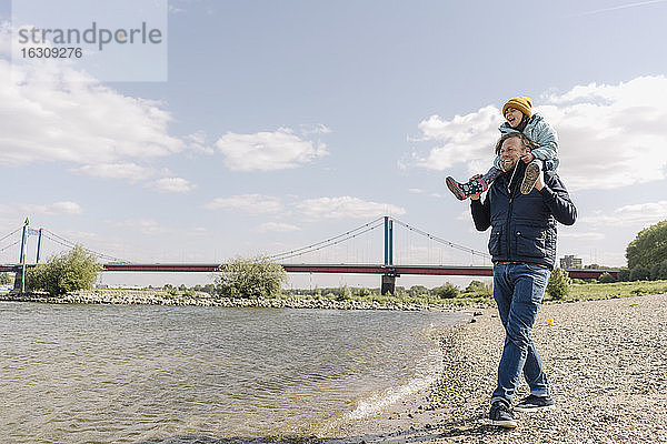 Vater  der seine Tochter auf der Schulter trägt  während er am Flussufer steht