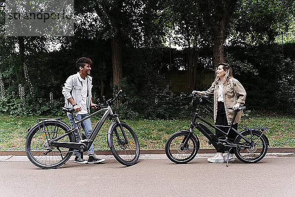 Lächelndes Paar steht mit Elektrofahrrädern auf der Straße