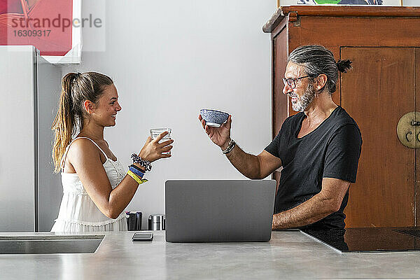 Lächelnder Vater und Tochter mit Getränken im Gespräch an der Küchentheke stehend