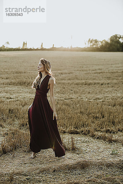 Unbekümmerte Frau steht in einem Feld und hält ihr Kleid