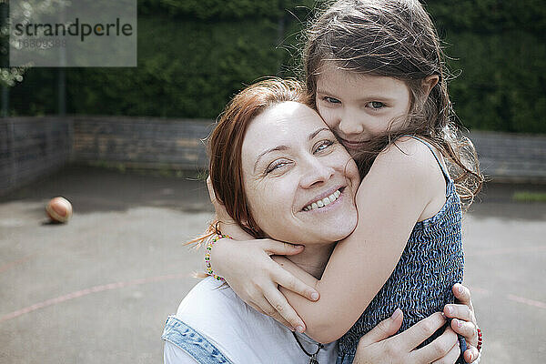 Mädchen umarmt lächelnde Mutter am Basketballplatz im Hinterhof