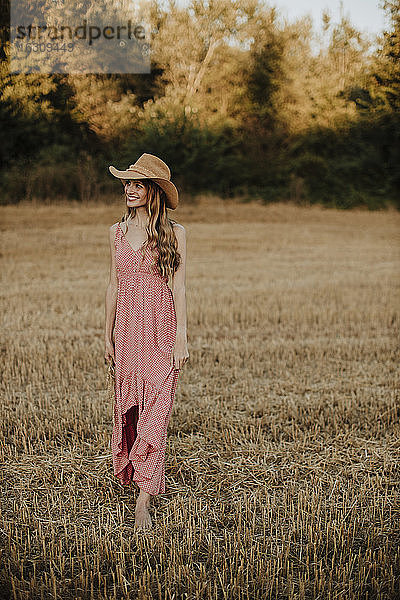 Frau im Kleid schaut weg  während sie bei Sonnenuntergang in einem Weizenfeld spazieren geht