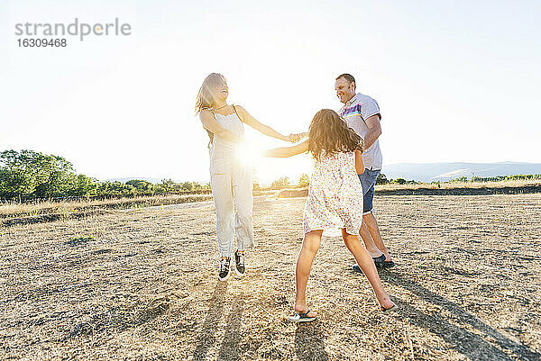 Fröhliche Eltern spielen mit ihrer Tochter auf dem Land gegen den klaren Himmel an einem sonnigen Tag