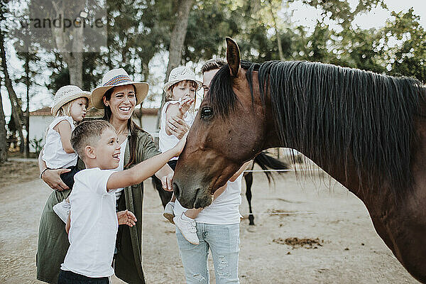 Fröhliche Eltern mit Kindern  die ein Pferd berühren  während sie im Freien stehen