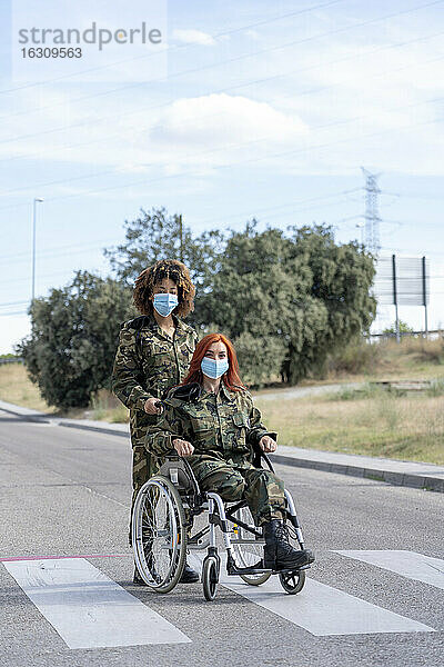 Eine Soldatin hilft einem im Rollstuhl sitzenden Offizier  während sie eine Gesichtsschutzmaske trägt.