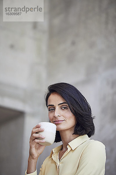 Nahaufnahme einer selbstbewussten Geschäftsfrau  die eine Kaffeetasse an die Wand eines Büros hält