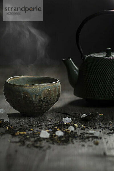 Japanische Teekanne und Schale mit Teeblättern auf Holztisch  Studioaufnahme