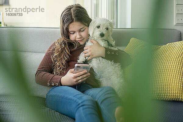 Mädchen benutzt Smartphone und hält Hund auf Sofa
