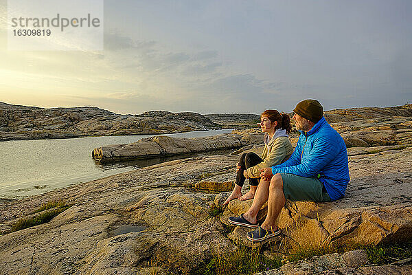 Schweden  Bezirk Vastra Gotaland  Grebbestad  Mann und junges Mädchen sitzen zusammen auf Küstenfelsen im Tjurpannans Naturreservat