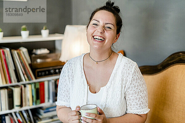 Fröhliche  üppige junge Frau  die einen Kaffeebecher hält  während sie in einem Café sitzt