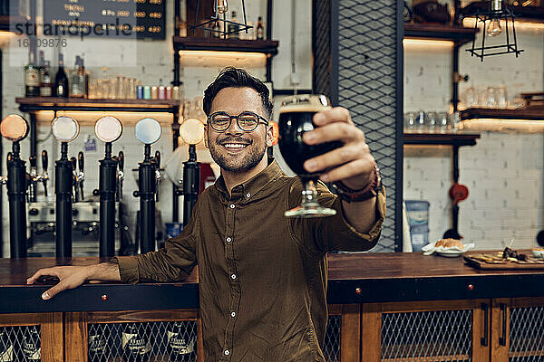 Porträt eines lächelnden Mannes  der sein Bierglas in einer Kneipe hebt