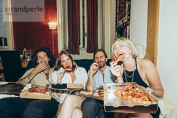 Glückliche Freunde genießen eine Pizza auf dem Sofa während einer Party zu Hause