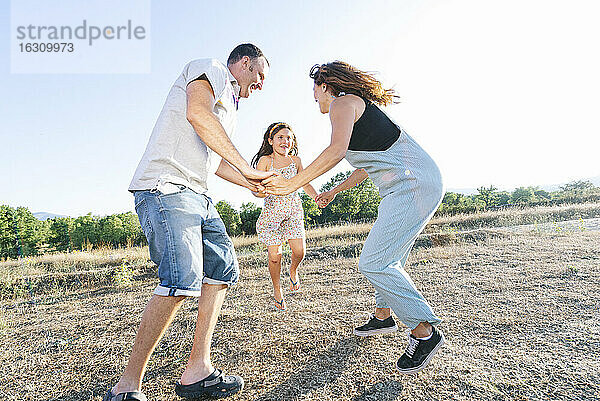 Fröhliche Eltern spielen mit ihrer Tochter an Land gegen den klaren Himmel