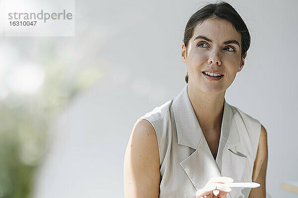 Nachdenkliche Frau schaut weg  während sie einen digitalisierten Stift im Büro hält
