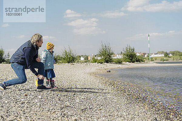Vater und Tochter betrachten den Fluss  während sie in der Nähe des Ufers einen Kieselstein ins Wasser werfen