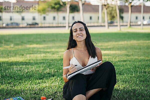Lächelnde Frau  die im Gras sitzend in einem öffentlichen Park malt