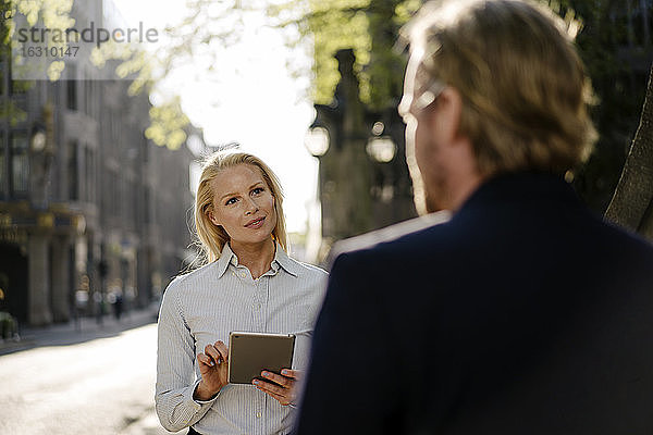 Geschäftsfrau  die ein digitales Tablet hält  während sie einen Geschäftsmann ansieht und in der Stadt diskutiert