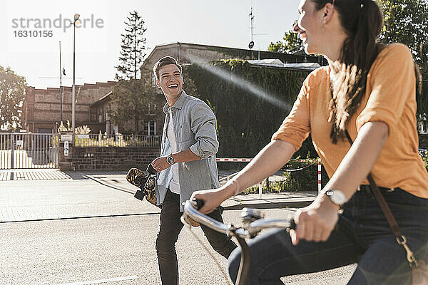 Fröhlicher junger Mann  der seine Freundin beim Fahrradfahren auf der Straße in der Stadt an einem sonnigen Tag beobachtet