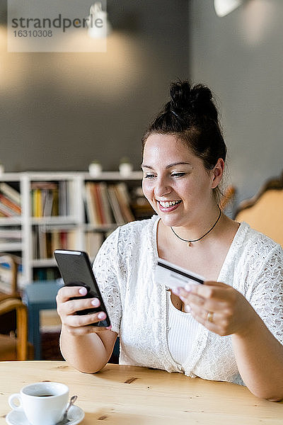 Lächelnde üppige Frau beim Online-Shopping über Handy in einem Café