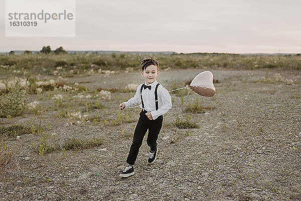 Junge mit herzförmigem Ballon läuft auf Feld gegen Himmel