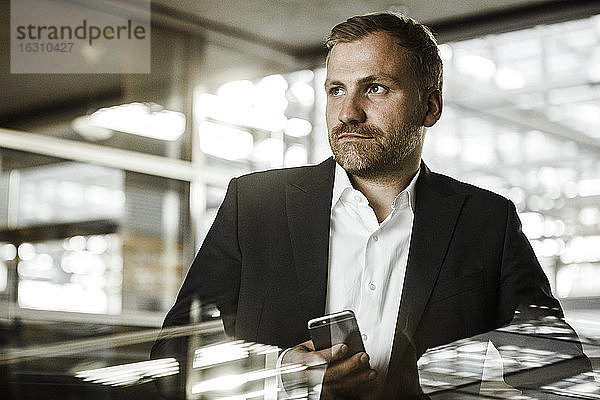 Porträt eines Geschäftsmannes mit Smartphone  der zur Seite schaut