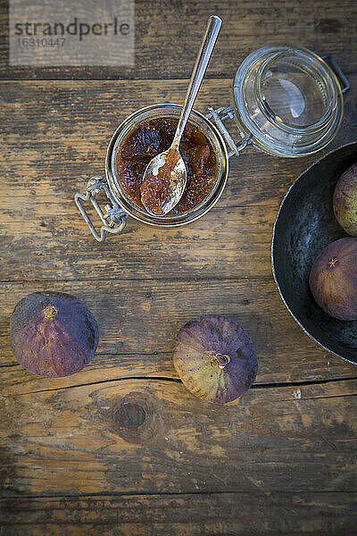 Vier Feigen (Ficus carica) und ein Glas mit Feigenmarmelade auf einem Holztisch  Studioaufnahme