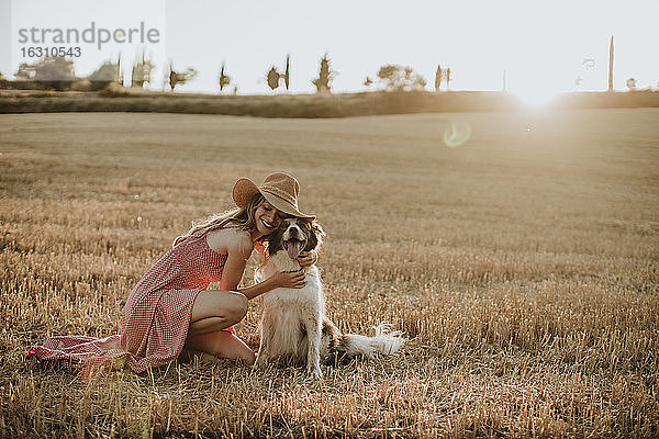 Frau umarmt Border Collie Hund in Weizenfeld bei Sonnenuntergang