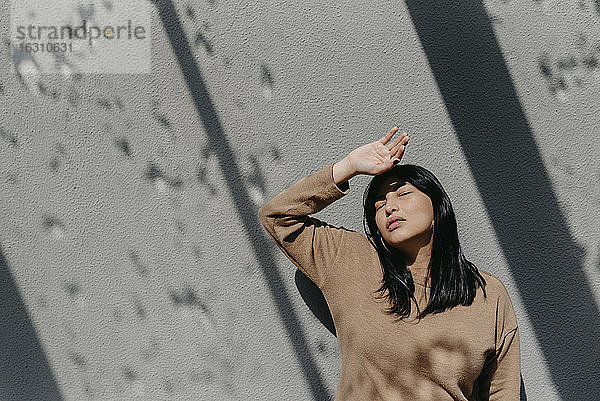 Schöne Frau  die ihre Augen abschirmt  während sie an einer Betonwand an einem sonnigen Tag steht