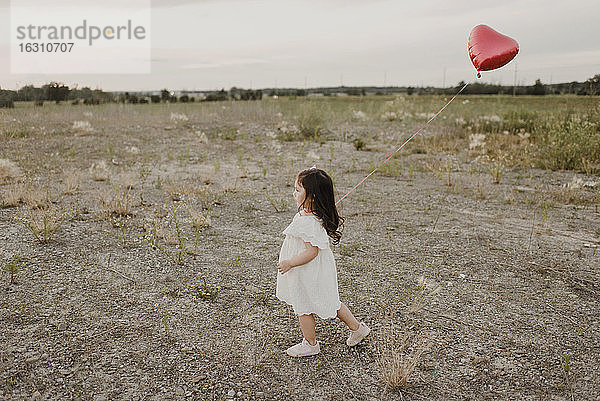 Nettes Mädchen mit Herzform Ballon zu Fuß in Feld